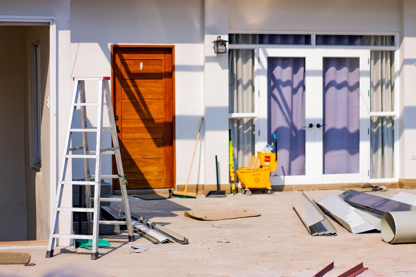 Hausmeister bei Außenarbeiten mit Leiter und Gerät vor dem Eingang eines Objekts